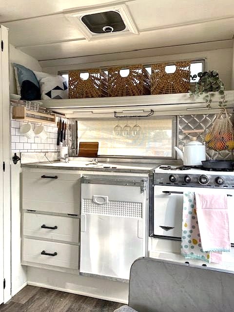 Vintage trailer kitchen with white cabinets, retro stove, woven baskets and tea towels