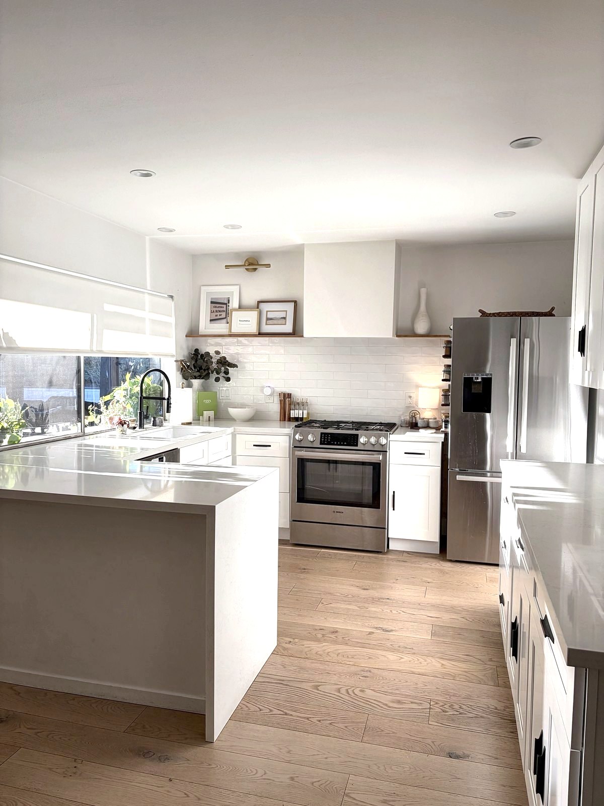 Sunlit white kitchen with waterfall peninsula, subway tile, range hood and styled open shelves