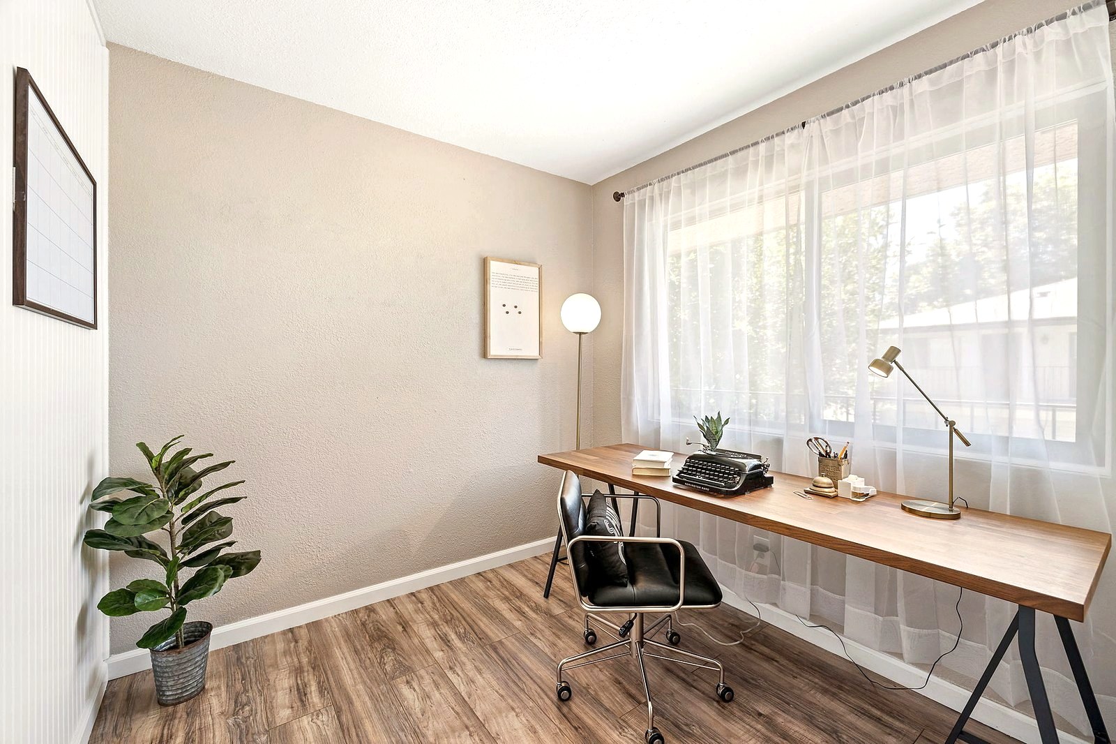 Home office with a long wood desk, typewriter and sheer window curtains