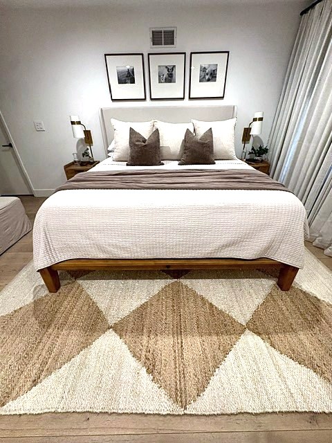 Primary bedroom with upholstered headboard, framed portraits, brass sconces and a diamond jute rug