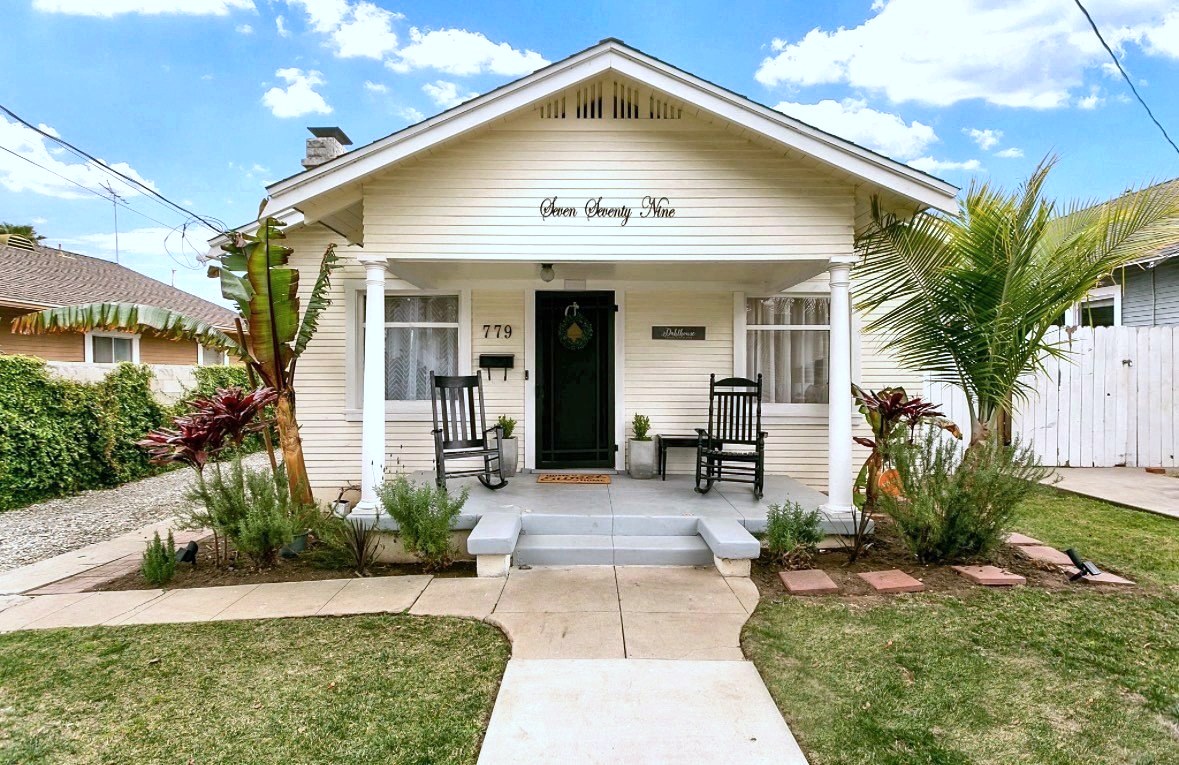 Cream vintage bungalow with a black front door, rocking chairs on the porch and tropical plantings
