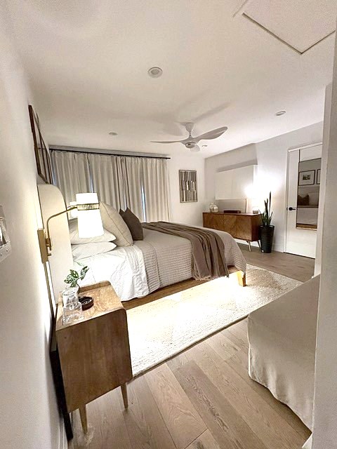 Primary bedroom at dusk with glowing sconce, walnut nightstand and dresser