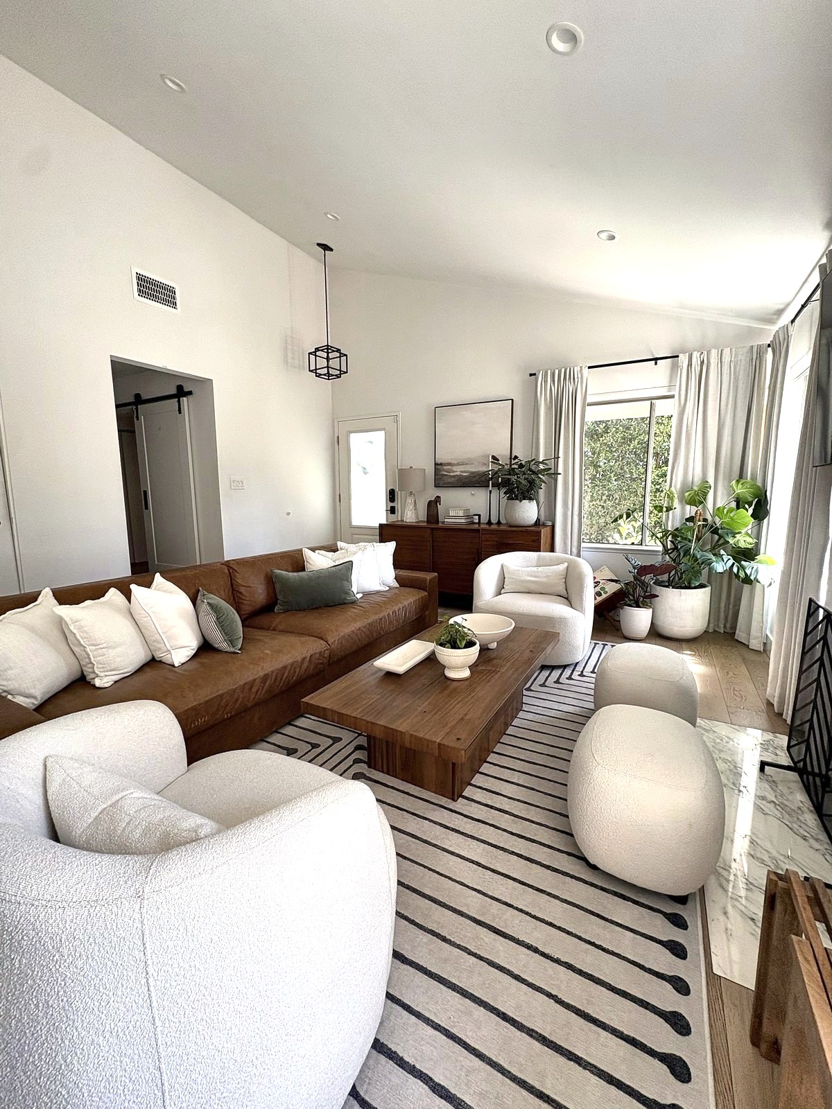 Sunny living room with leather sectional, boucle swivel chairs, walnut coffee table and potted plants