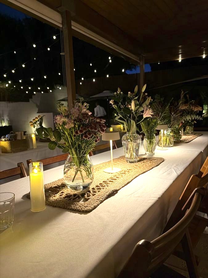 Candlelit dinner table with wildflowers in glass vases, jute runner and string lights